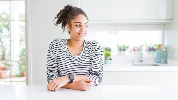 Beautiful african american woman with afro hair wearing casual striped sweater looking away to side with smile on face, natural expression. Laughing confident.