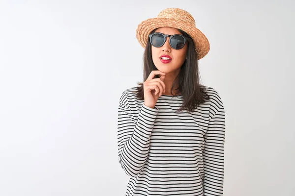 中国女人戴着条纹T恤帽太阳镜站在孤立的白色背景上 手放在下巴上思考着问题 沉思着表情 脸上挂着沉思的笑容 怀疑的概念 — 图库照片