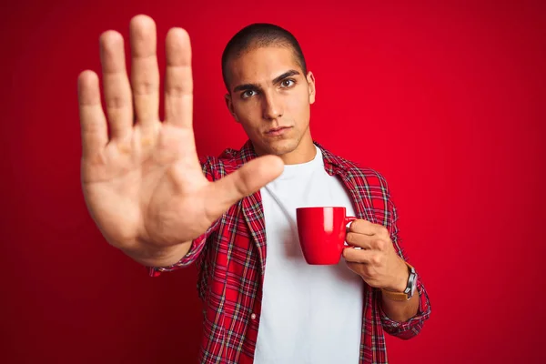 年轻英俊的男子 身穿衬衫 在红隔离的背景下喝着一杯咖啡 张开双臂 严肃而自信地做着止步手势 做着防守动作 — 图库照片