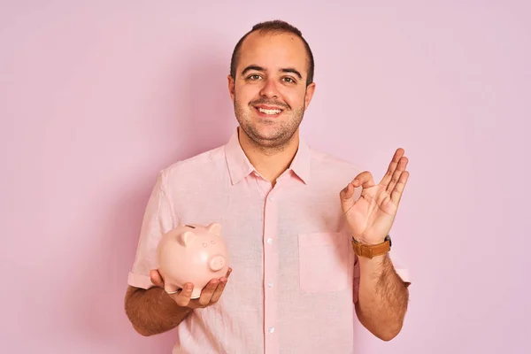 Junger Mann Hält Sparschwein Über Isoliertem Rosa Hintergrund Und Tut — Stockfoto