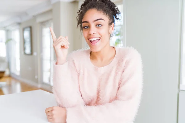 Beautiful young african american woman with afro hair with a big smile on face, pointing with hand and finger to the side looking at the camera.