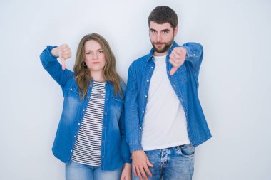 İzole edilmiş beyaz arka planda birlikte duran genç ve güzel bir çift mutsuz ve kızgın görünüyor. Reddedilmiş ve olumsuz bir hareket sergiliyor. Kötü ifade.