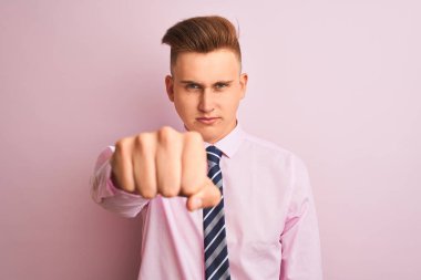 Gömlek ve kravat takan genç yakışıklı iş adamı pembe arka planda duruyor. Yumruk yumruğa dövüşmek, agresif ve öfkeli saldırı, tehdit ve şiddet.