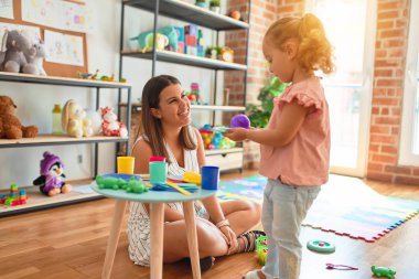 Güzel öğretmen ve sarışın yeni yürümeye başlayan kız anaokulunda plastik meyve, sebze ve yemekle oynuyor.