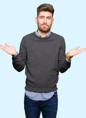 Genç yakışıklı zarif adam clueless ve şaşkın ifadeyle kollar ve eller kaldırdı. Şüphe kavramı.