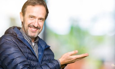 Orta yaş yakışıklı adam giyen kış işaretçi el yanında kat ve açık palm, mutlu ve kendine güvenen reklam gülümseyen sunulması