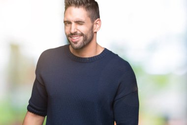 Seksi bir ifadeyle, neşeli ve mutlu yüzünü kameraya bakarak göz kırpıyor izole arka plan üzerinde kazak giyen genç yakışıklı adam.