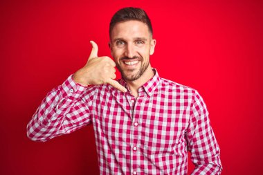 Kırmızı izole edilmiş arka plan üzerinde genç yakışıklı adam telefonla el ve parmaklarıyla gülümseyerek konuşuyor. İletişim kavramları.