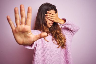 Pembe izole edilmiş arka plan üzerinde duran genç ve güzel bir kadın ellerle gözlerini kapatıyor ve üzgün ve korku ifadeleriyle jestleri durduruyor. Utanç verici ve olumsuz bir kavram..