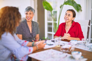 Orta yaşlı kadınlarla buluşup, öğle yemeği yiyip, kahve içiyorlar. Olgun arkadaşlar mutlu bir şekilde gülümsüyor. Güneşli bir günde evde akıllı telefon kullanıyorlar.