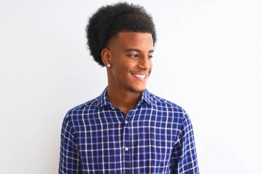 Genç Afro-Amerikalı bir adam, günlük gömlekler giyip izole edilmiş beyaz arka planda duruyor. Yüzünde gülümseme, doğal bir ifade ile yan yana bakıyor. Kendinden emin gülen.