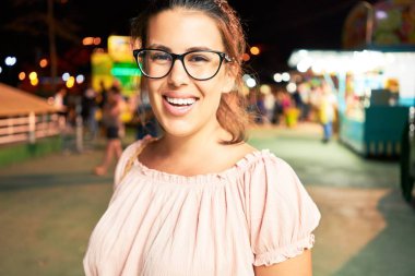 Gözlük takan genç ve güzel bir kadın gecenin ışıklarında mutlu ve heyecanlı bir şekilde gülümsüyor.