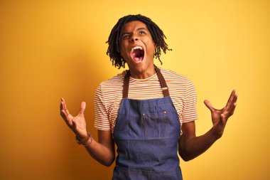 Sarı arka plan üzerinde önlük giyen Afro-Amerikalı barista adam sinirli bir şekilde bağırıyor, bağırıyor ve agresif bir ifade takınıyor. Hayal kırıklığı konsepti.