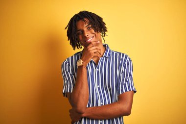 Rastgele çizgili tişörtlü Afro adam izole edilmiş sarı arka planda kameraya bakıyor kollarını kavuşturup gülümseyerek ve çenesini kaldırarak bakıyor. Olumlu düşünüyorum..