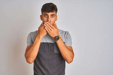 İzole edilmiş beyaz arka planda duran günlük tişört giyen genç Hintli adam yanlışlıkla ağızlarını kapatarak şok geçirdi. Gizli konsept.