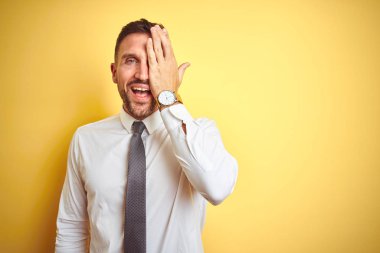 Sarıya boyanmış zarif beyaz gömlek giyen yakışıklı iş adamı bir gözünü elinle kapatıyor, yüzünde kendine güvenen bir gülümseme ve sürpriz bir duygu var..