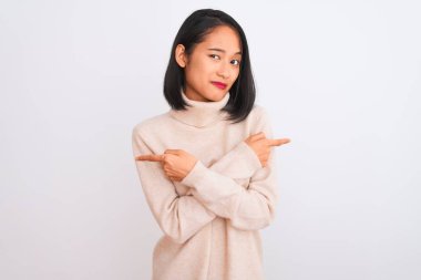 Balıkçı yaka kazak giyen genç bir kadın izole edilmiş beyaz arka planda duruyor. İki tarafı da işaret ediyor. Farklı yönlerden.