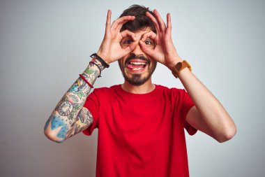 İzole edilmiş beyaz arka plan üzerinde duran kırmızı tişörtlü genç bir adam dürbün gibi dil çıkartıyor, gözler parmaklarından bakıyor. Çılgın ifade.