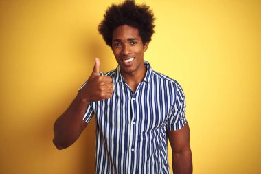Afro saçlı, çizgili tişörtlü, izole edilmiş sarı arka planda duran Amerikalı bir adam mutlu bir el hareketi yapıyor. Kameraya bakıp başarıyı gösteren ifade onaylanıyor.