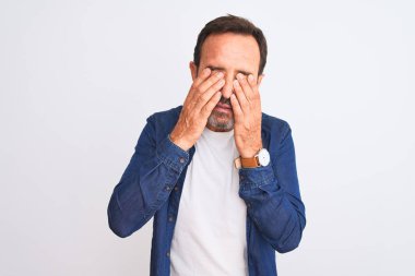 Mavi kot gömlek giyen orta yaşlı yakışıklı adam izole edilmiş beyaz arka plan üzerinde duruyor yorgunluk ve baş ağrısı için gözlerini ovuşturuyor, uykulu ve yorgun bir ifade takınıyor. Görüş sorunu
