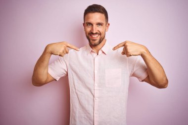 Pembe izole edilmiş arka planda zarif bir yaz gömleği giyen yakışıklı bir genç. Yüzünde bir gülümseme, kendini gururla ve mutlu bir şekilde gösteren bir adam..