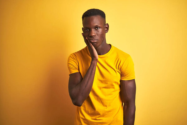 Young african american man wearing casual t-shirt standing over isolated yellow background thinking looking tired and bored with depression problems with crossed arms.