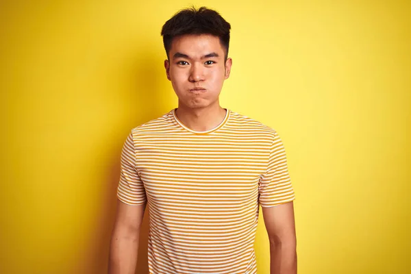 若いアジア系中国人の男性は Tシャツを着て 黄色の背景が面白い顔で頬をむき出しの上に立っている 口は空気で膨脹し 狂気の表現 — ストック写真