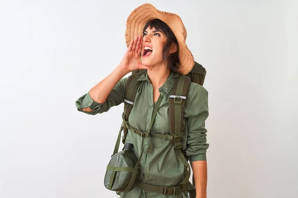 Hiker woman wearing backpack hat and water canteen over isolated white background shouting and screaming loud to side with hand on mouth. Communication concept.