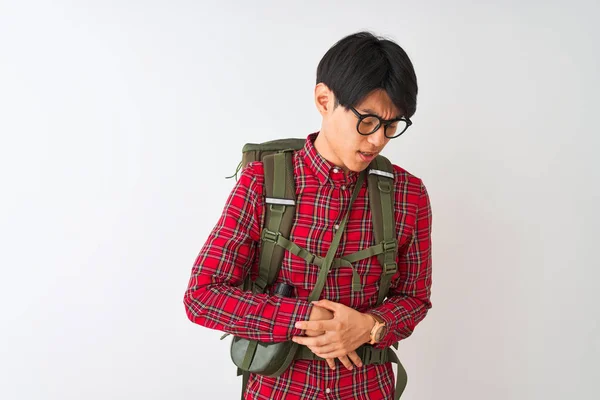 Chinese hiker man wearing backpack canteen glasses over isolated white background with hand on stomach because indigestion, painful illness feeling unwell. Ache concept.