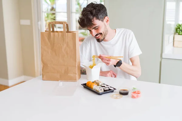 Young man eating sushi asian food and noodles using choopsticks