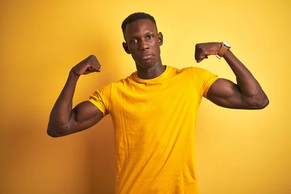 孤立した黄色の背景の上に立つカジュアルなTシャツを着ている若いアフリカ系アメリカ人の男性は腕の筋肉を誇りに思って笑顔を見せる フィットネスコンセプト — ストック写真