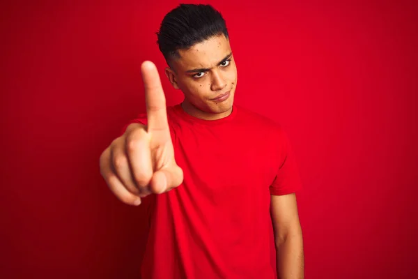 年轻的巴西男子穿着T恤 站在孤立的红色背景上 手指头翘起 满脸怒容 毫无表情 — 图库照片