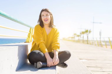 Güzel genç kadın deniz tarafından bir gezinti üzerinde oturan gülümseyen 