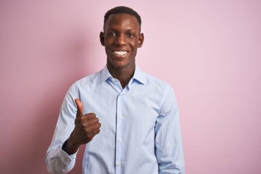 Mavi şık gömlekli Afro-Amerikan bir adam pembe arka planda dikiliyor ve elleriyle mutlu bir jest yapıyor. Kameraya bakıp başarıyı gösteren ifade onaylanıyor.