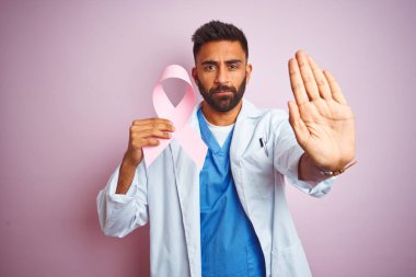 Kanser kurdelesi tutan genç Hintli doktor pembe arka planda duruyor. Açık elle dur işareti yapıyor. Ciddi ve kendinden emin bir ifadeyle, savunma hareketi yapıyor.