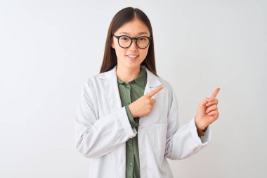 Young chinese scientist woman wearing coat and glasses over isolated white background smiling and looking at the camera pointing with two hands and fingers to the side.