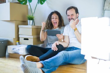 Orta yaşlı çift tablet kullanarak yeni bir eve taşınıyor. Gururla bağırıyor, zaferi ve başarıyı kutluyor. Çok heyecanlı, coşkulu bir duygu.