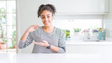 Afro saçlı, sıradan çizgili süveter giyen, elleri büyük ve büyük boy işareti gösteren güzel Afrikalı Amerikalı kadın. Ölçü sembolü. Kameraya bakıp gülümsüyor. Ölçüm konsepti.