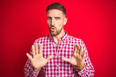 Kırmızı arkaplan üzerinde genç yakışıklı bir adam. Avuçlarını hareket ettiriyor. Korkmuş ve iğrenç bir ifadeyle reddediyor. Dur ve yasakla.