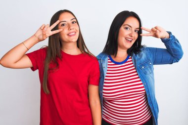 İzole edilmiş beyaz arka plan üzerinde dikilen genç ve güzel kadınlar barış sembolü yapıyorlar. Yüzlerinde parmaklar, gülümseyerek zafer gösteriyorlar.