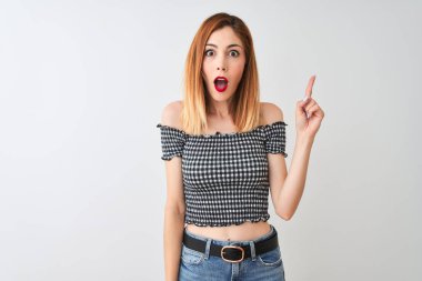 Güzel kızıl saçlı kadın, izole edilmiş beyaz arka planda duran günlük tişörtler giyip başarılı bir fikir işaret ediyor. Heyecanlı ve mutlu. Bir numara..