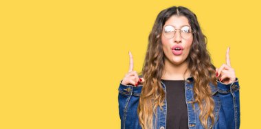 Gözlük ve denim ceket giyen genç güzel kadın hayrete ve yukarıya bakıyor ve parmakları ile işaret ve silah kaldırdı şaşırttı.