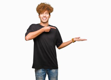 Siyah t-shirt giyen afro saç ile genç yakışıklı adam hayran ve kamera gülümseyen el ile sunmak ve parmak ile işaret.