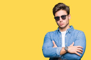 Genç yakışıklı adam izole arka plan şüpheci ve sinir, onaylamayan ifade yüz çapraz kolları üzerinde güneş gözlüğü takıyor. Negatif kişi.