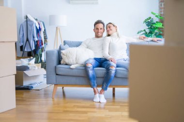 Karton kutular etrafında yeni evde kanepede oturan köpek ile genç güzel çift