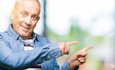 Gülen ve iki el ve parmak tarafına işaret kamera bakarak kot ceket giyen yakışıklı kıdemli adam.