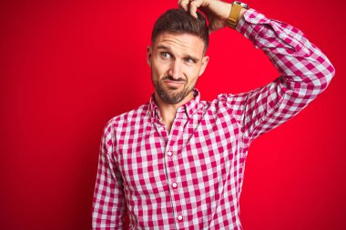 Kırmızı izole edilmiş arka plan üzerindeki genç yakışıklı adam soru sorup kafasını karıştırıyor. Şüpheyle kararsız, kafa kafaya düşünerek. Düşünceli kavram.