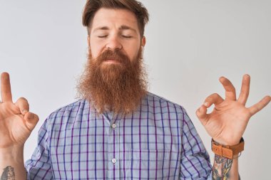 Kızıl saçlı İrlandalı adam kablosuz kulaklık kullanarak müzik dinliyor izole beyaz arka planda rahatlıyor ve gözleri kapalı gülümsüyor parmaklarıyla meditasyon hareketi yapıyor. Yoga konsepti.