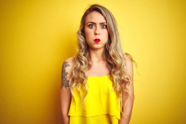 Sarı izole edilmiş arka planda duran tişört giyen genç saldırgan kadın komik yüzlü yanakları şişiriyor. Havayla şişmiş ağız, çılgın bir ifade..