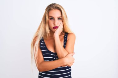 Genç ve güzel bir kadın, günlük çizgili tişört giyip izole edilmiş beyaz arka plan üzerinde duruyor. Kollarını kavuşturup depresyondan sıkılmış ve yorgun görünüyor..
